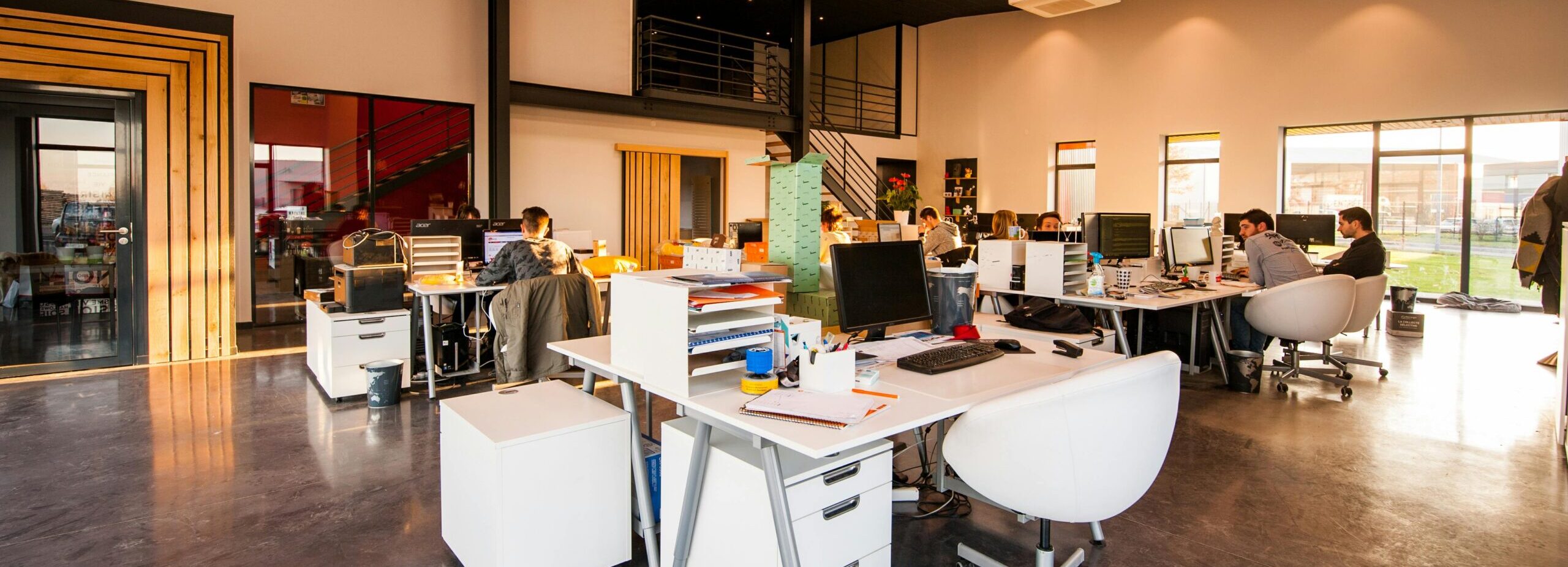 A spacious and modern open-plan office with natural lighting and employees working at desks.